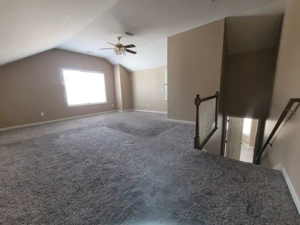 an empty room with a chandelier fan and windows