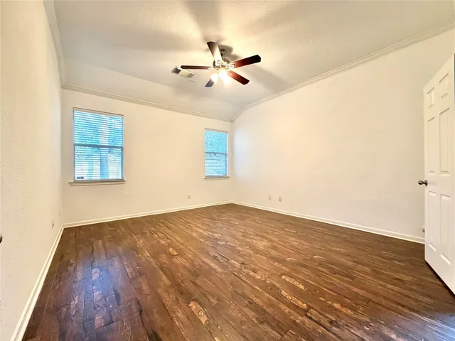 an empty room with wooden floor fan and windows