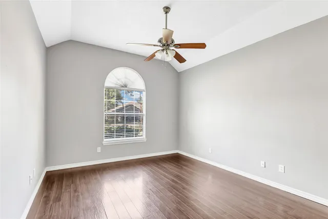 an empty room with wooden floor chandelier fan and windows