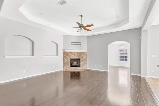 an empty room with wooden floor a ceiling fan a fireplace and windows