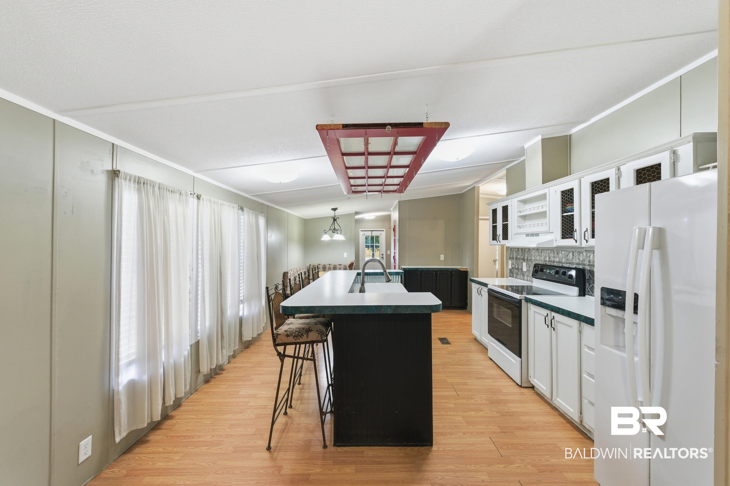 926 Tumbling Lane Atmore, AL 36502 - Photo 17 of 56 Kitchen featuring wood-finish flooring, white cabinetry, a central island with integrated sink, and a tiled backsplash