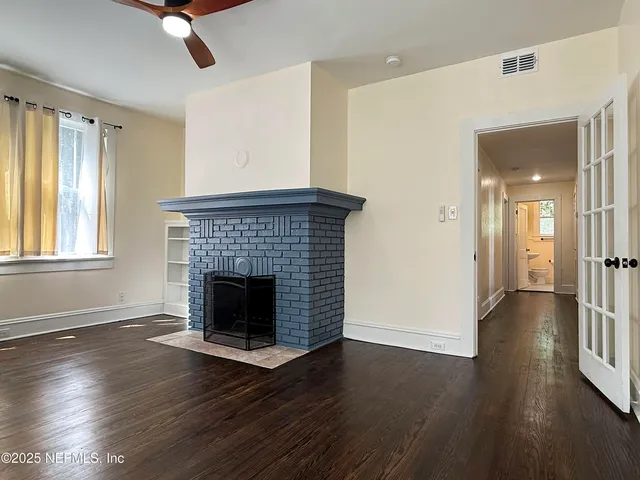 a view of an empty room with wooden floor fireplace and a window