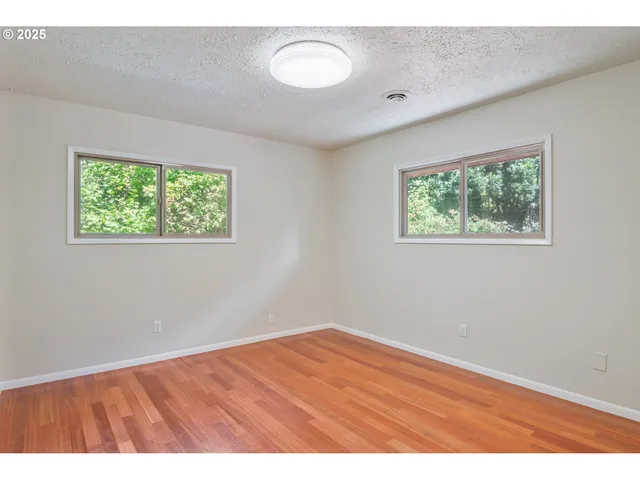 a view of an empty room with a window and wooden floor