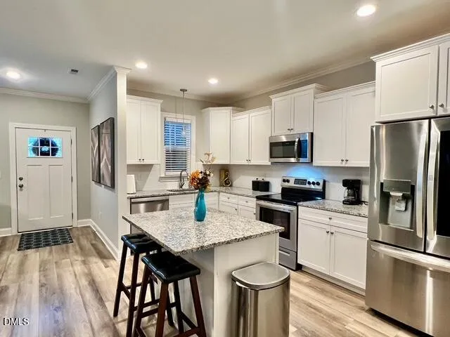 a kitchen with stainless steel appliances granite countertop a refrigerator a stove top oven a sink dishwasher and white cabinets with wooden floor