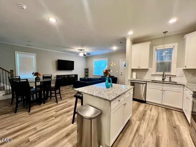 a large white kitchen with cabinets a sink dishwasher a stove and a dining table with wooden floor