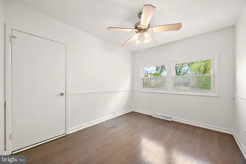 an empty room with wooden floor fan and windows