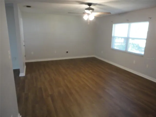 an empty room with wooden floor chandelier fan and windows