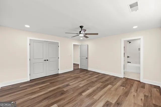a view of an empty room with wooden floor and a ceiling fan