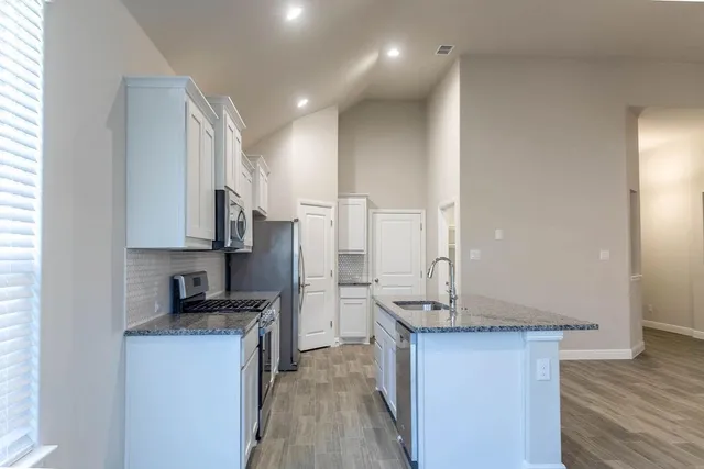 a kitchen with stainless steel appliances granite countertop a sink a stove a refrigerator cabinets and living room view