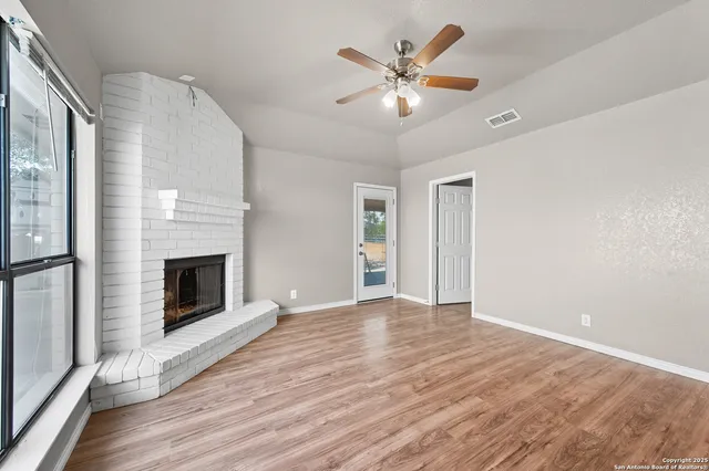 an empty room with wooden floor fireplace and windows