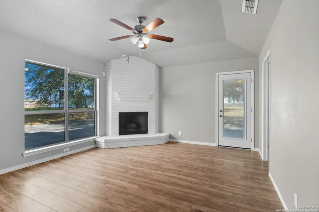 an empty room with wooden floor a ceiling fan and windows