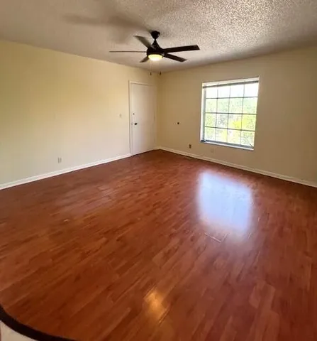 an empty room with wooden floor ceiling fan and windows