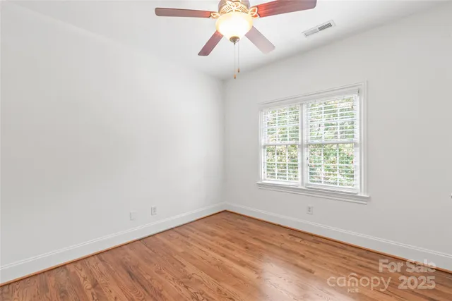 an empty room with chandelier fan and windows