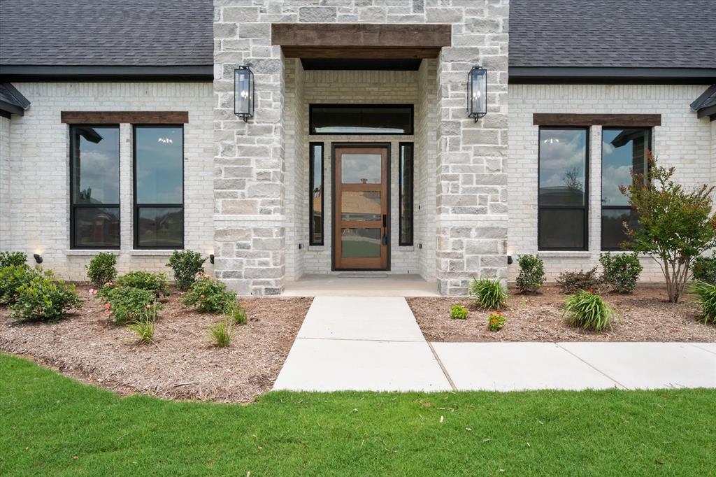 6610 Waggoner Way Midlothian, TX 76065 - Photo 4 of 40 Modern facade featuring a wooden entry door with frosted glass panels, surrounded by a light-toned brick and stone veneer