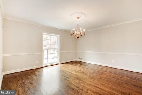 an empty room with wooden floor chandelier and windows