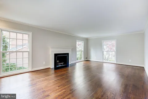 an empty room with wooden floor fireplace and windows