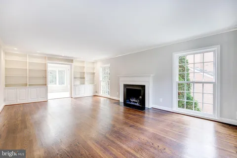an empty room with wooden floor fireplace and windows