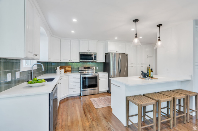 3813 North Foothill Drive Provo, UT 84604 - Photo 16 of 71 Modern kitchen featuring white cabinetry, a teal vertical tile backsplash, stainless steel appliances, a white countertop, and wood-finish flooring