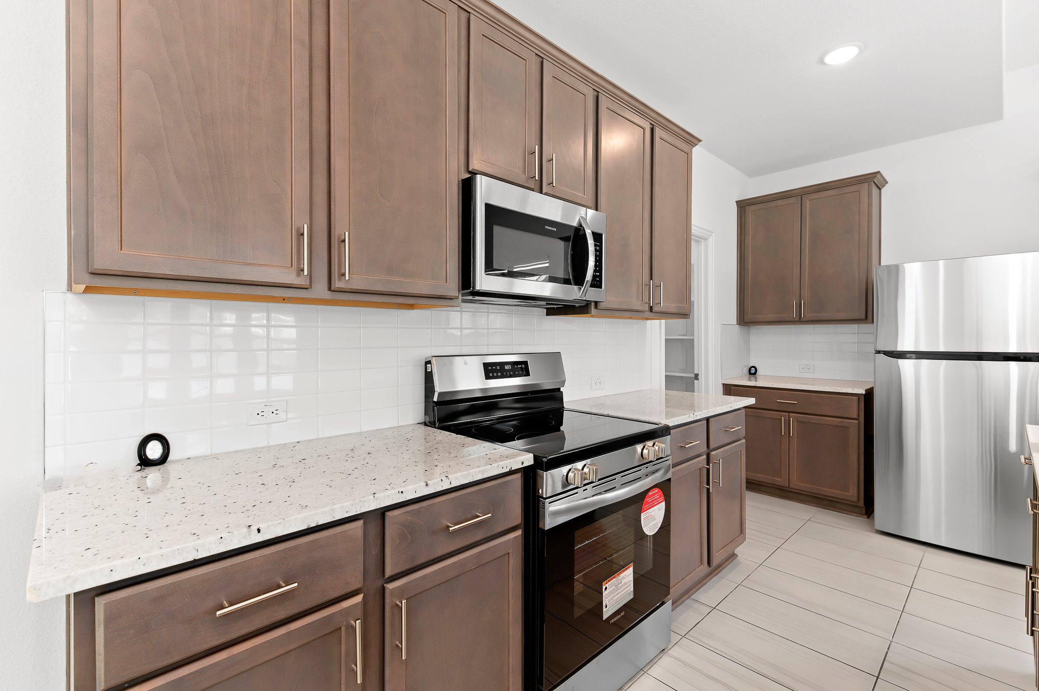 1128 Ridge Runner Drive Georgetown, TX 78628 - Photo 10 of 40 Kitchen with stainless steel appliances, light stone countertops, backsplash, dark wood finish cabinets, and light tile patterned floors