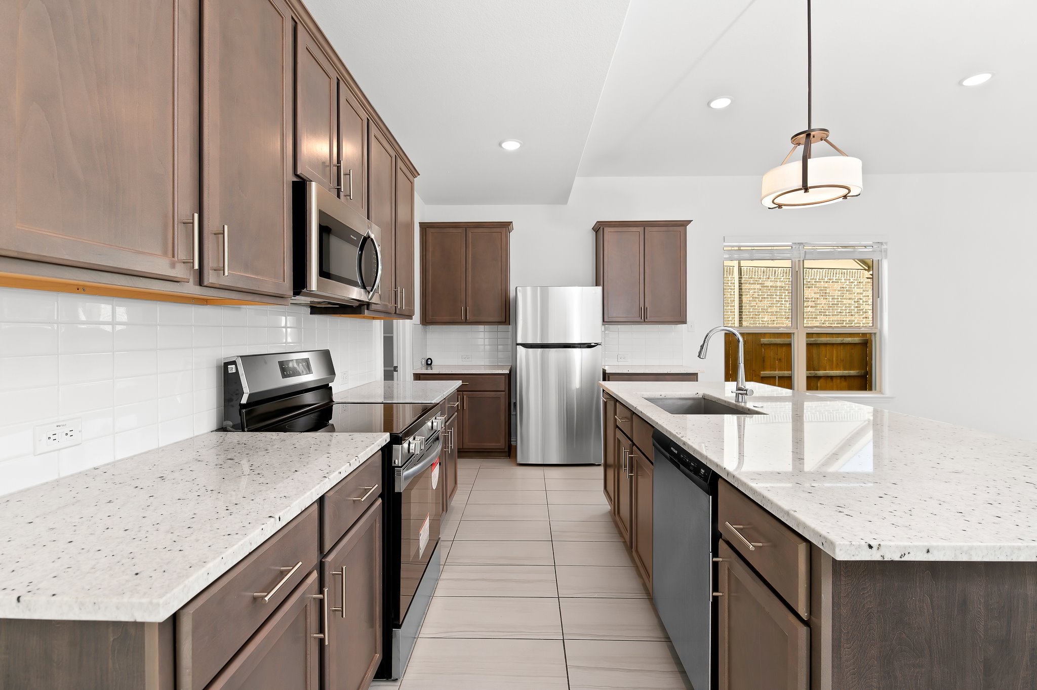 1128 Ridge Runner Drive Georgetown, TX 78628 - Photo 9 of 40 Kitchen with stainless steel appliances, backsplash, a kitchen island with sink, light stone countertops, and decorative light fixtures