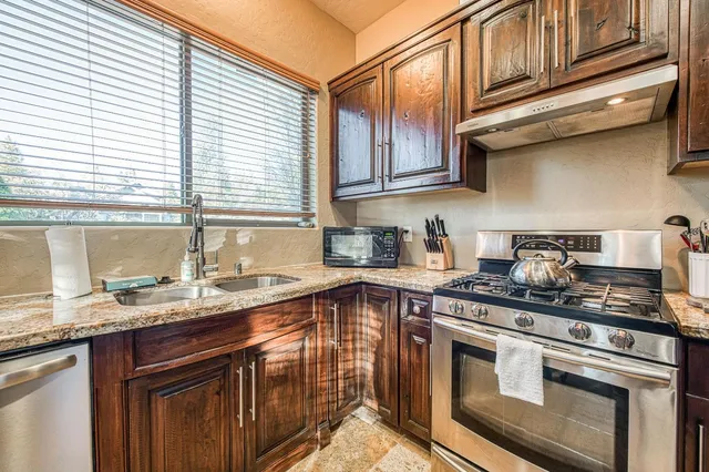 a kitchen with granite countertop a refrigerator a sink a stove and chairs