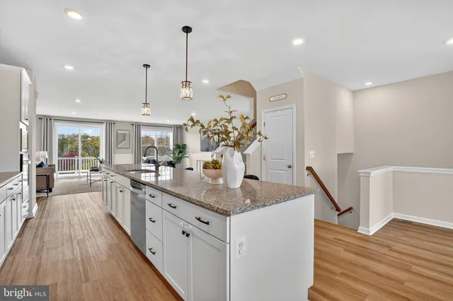 a kitchen with stainless steel appliances granite countertop a sink dishwasher a refrigerator and white cabinets with wooden floor