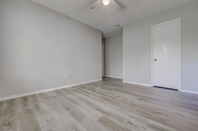 a view of an empty room with wooden floor and a ceiling fan