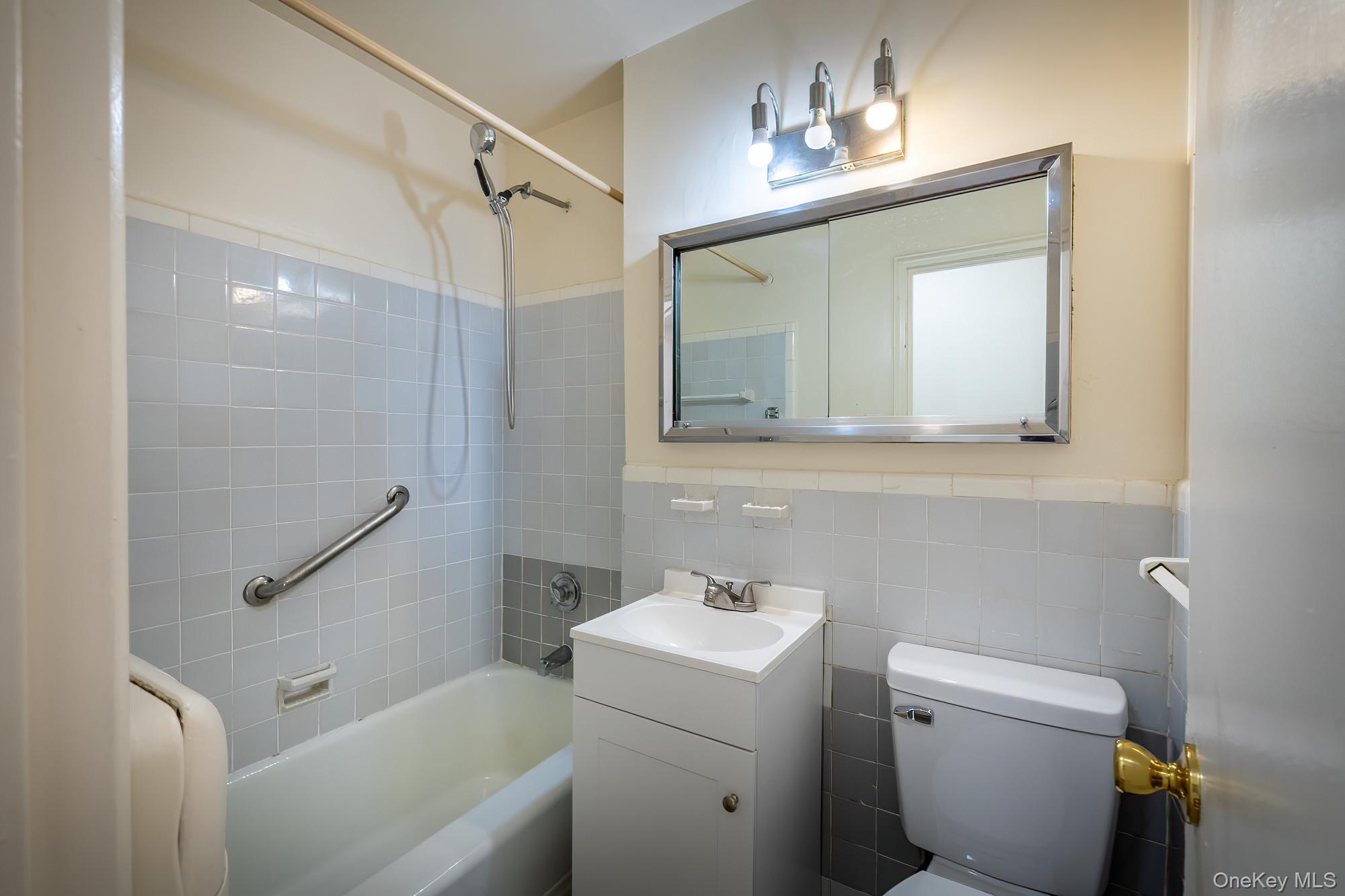 25 Knolls Crescent, Unit 8L Bronx, NY 10463 - Photo 15 of 21 Full bathroom featuring vanity, bathtub / shower combination, tile walls, and a wainscoted wall
