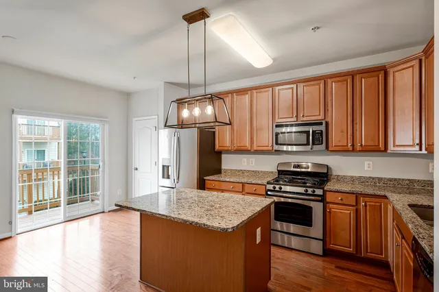 a kitchen with stainless steel appliances granite countertop a stove a sink dishwasher a refrigerator white cabinets and wooden floor