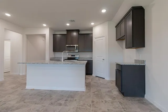 a large kitchen with stainless steel appliances a large counter top a stove a microwave a sink and a refrigerator