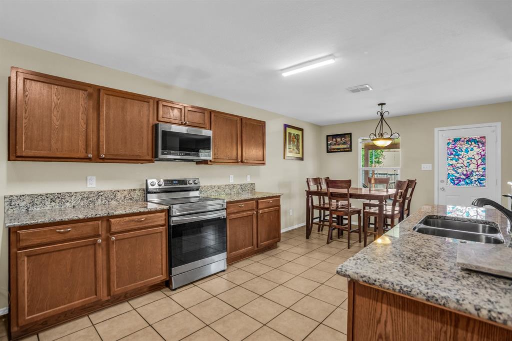 5718 Green Ivy Road Denton, TX 76210 - Photo 8 of 37 Kitchen featuring wood cabinetry, light-toned countertops, tile flooring, and stainless steel appliances