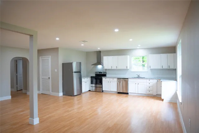 a large kitchen with stainless steel appliances granite countertop a refrigerator a sink dishwasher a stove and a large countertops with wooden floor
