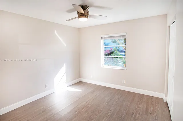 an empty room with wooden floor chandelier fan and windows