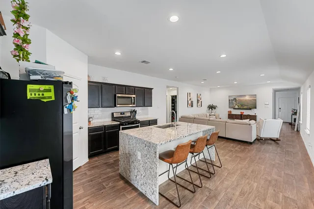 a kitchen with stainless steel appliances kitchen island granite countertop a refrigerator a stove a microwave oven a dining table and chairs with wooden floor