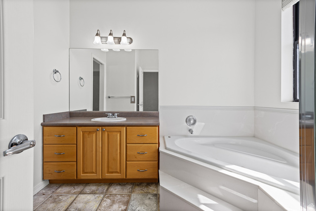 70 North Main Street, Unit 213 Bountiful, UT 84010 - Photo 12 of 15 Bathroom featuring a corner soaking tub, a single vanity with wood cabinetry, and a walk in shower to the left.