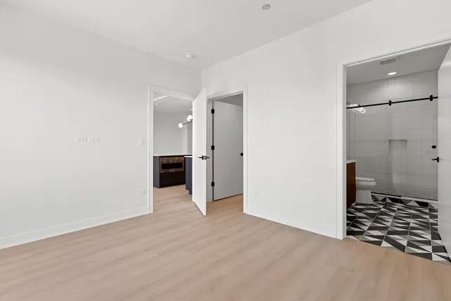 a view of an empty room with wooden floor and a kitchen