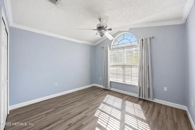 an empty room with wooden floor ceiling fan and windows