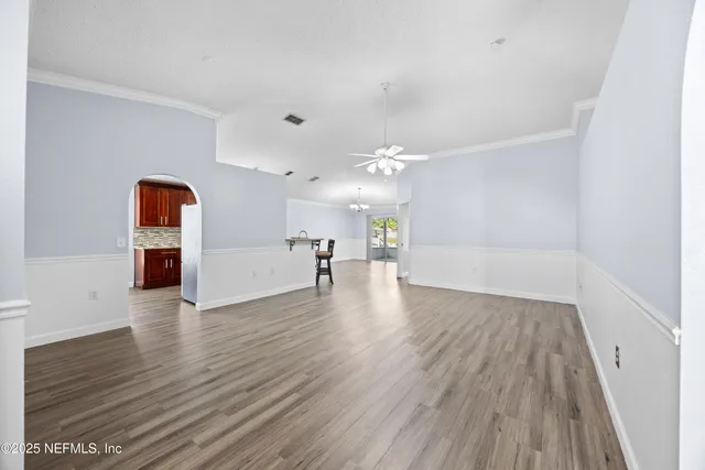 a view of an empty room with wooden floor kitchen view and a window