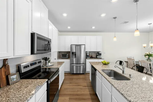 a kitchen with stainless steel appliances a dining table chairs refrigerator and microwave