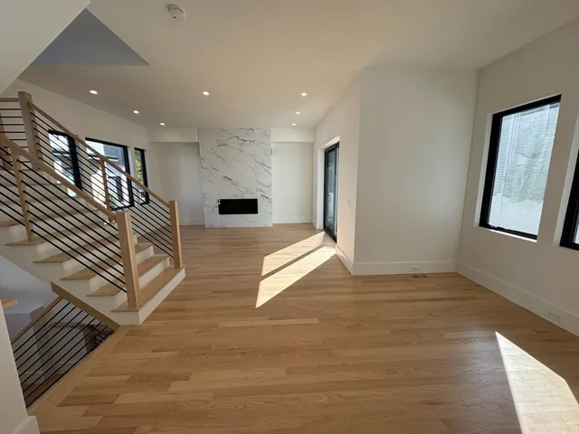 a view of an empty room and kitchen with wooden floor