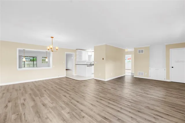 an empty room with wooden floor kitchen view and a window