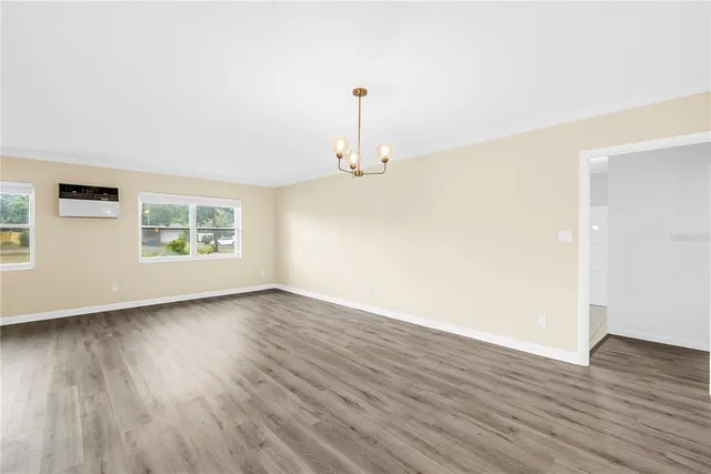 an empty room with wooden floor chandelier and windows
