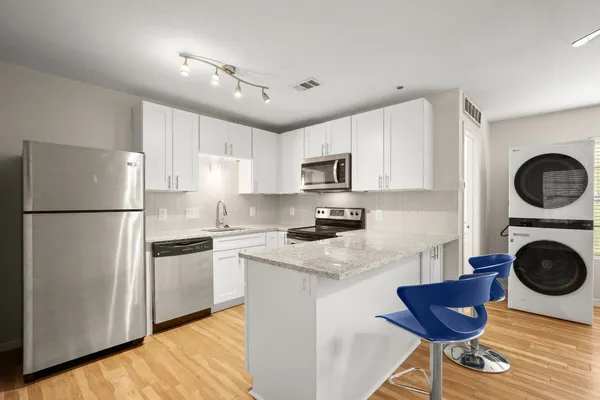 a kitchen with stainless steel appliances granite countertop a refrigerator a stove a sink dishwasher and white cabinets with wooden floor