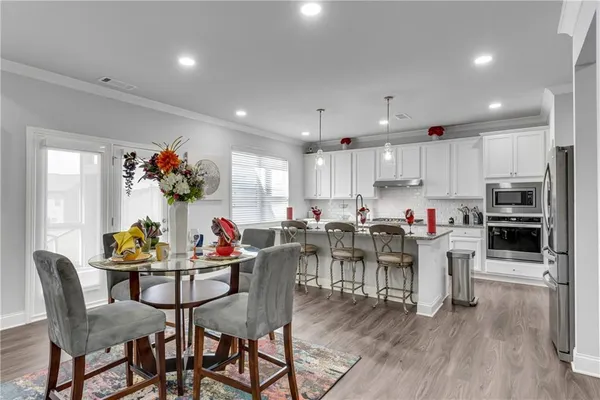 a kitchen with stainless steel appliances a microwave a stove a sink dishwasher a refrigerator and white cabinets with wooden floor