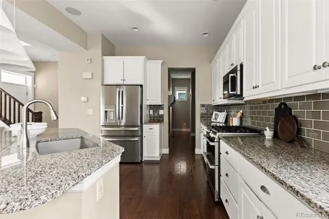 a kitchen with kitchen island granite countertop a stove a sink a refrigerator and white cabinets