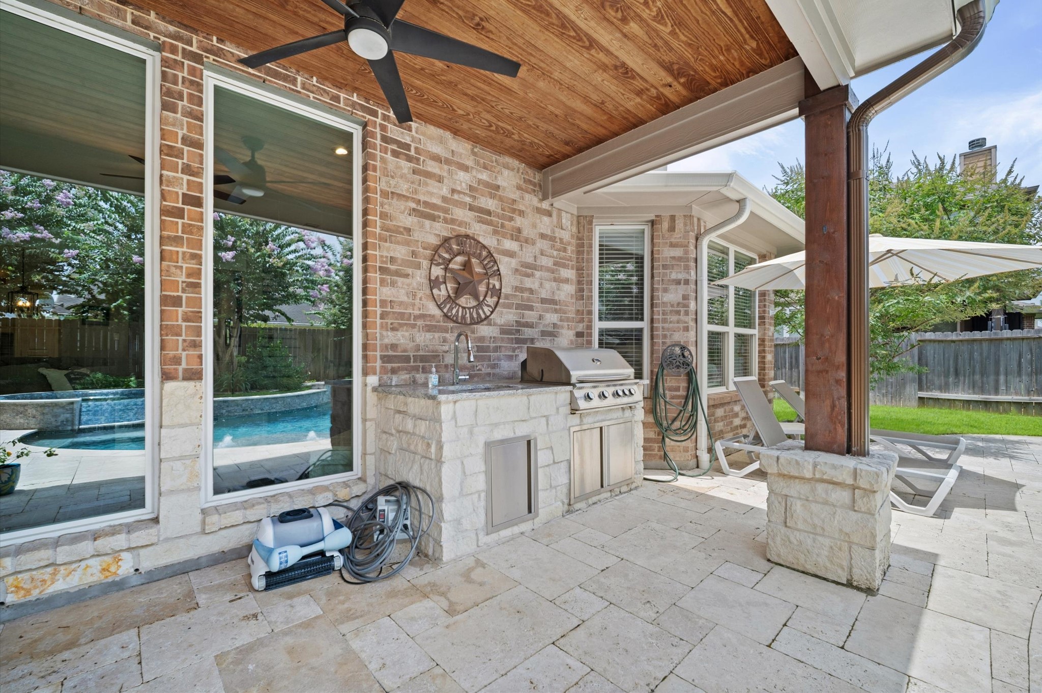 9507 Empress Crossing Drive Spring, TX 77379 - Photo 42 of 50 This outdoor space features a covered patio with a ceiling fan, a built-in grill with stone surround, and a view of the pool. Large windows provide natural light, and there's ample space for outdoor furniture and relaxation.