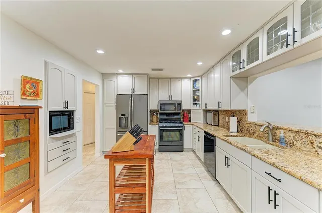 a kitchen with stainless steel appliances granite countertop a stove top oven a sink a refrigerator and white cabinets with wooden floor