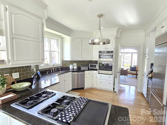 a kitchen with stainless steel appliances granite countertop a stove a sink dishwasher a refrigerator a dining table and chairs with wooden floor