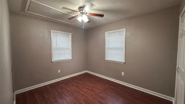 an empty room with wooden floor chandelier fan and windows