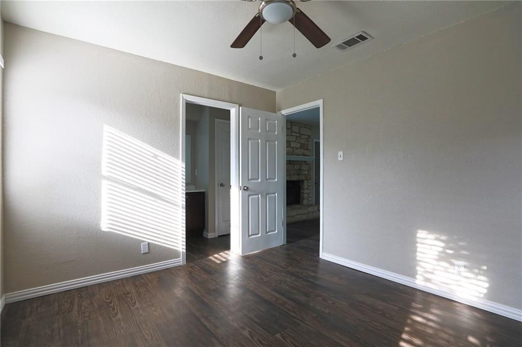 1410 Ransom Street Pflugerville, TX 78660 - Photo 19 of 22 Unfurnished bedroom with dark wood-style floors, ceiling fan, a fireplace with raised hearth, and a textured wall